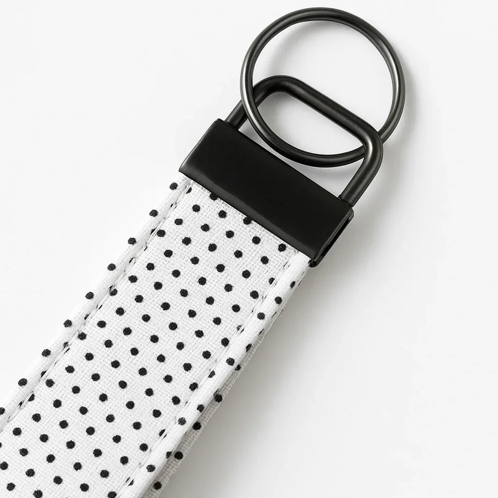 Close-up of a white canvas keychain fob with black polka dots and metal hardware