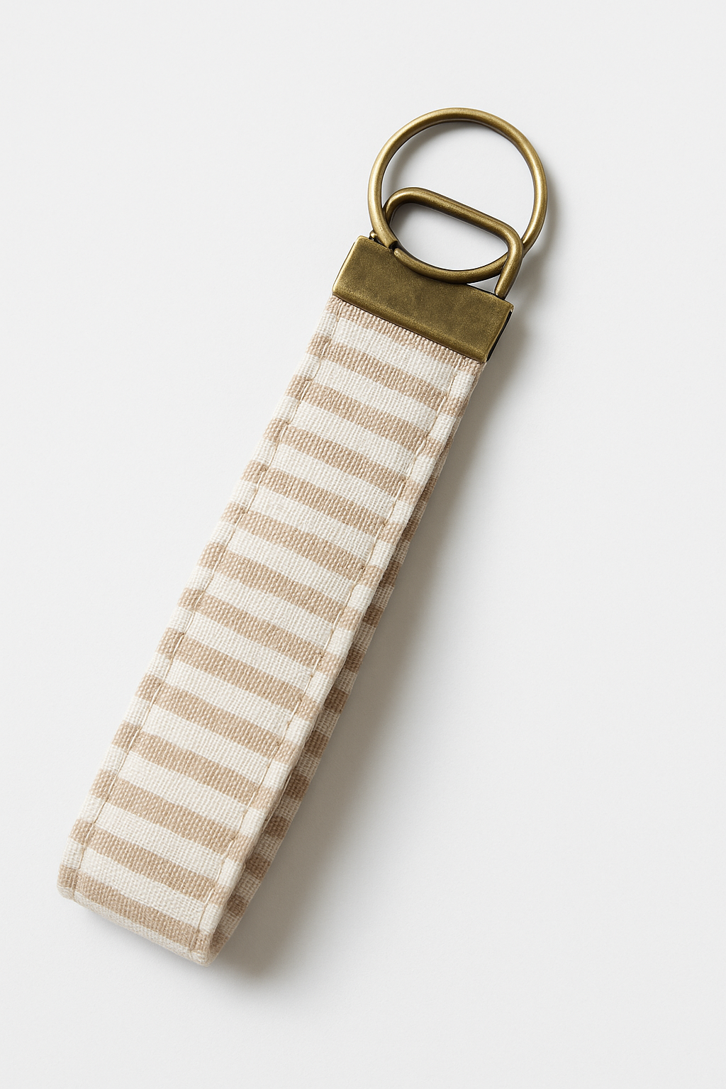 Beige and white striped fabric keychain fob with brass hardware on white background