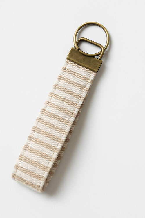 Beige and white striped fabric keychain fob with brass hardware on white background