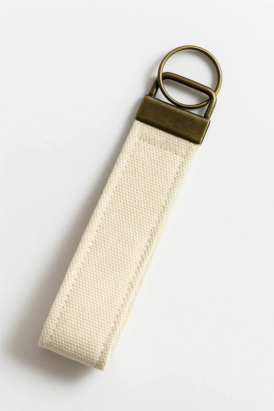 Neutral canvas wristlet keychain with antique brass hardware on white background