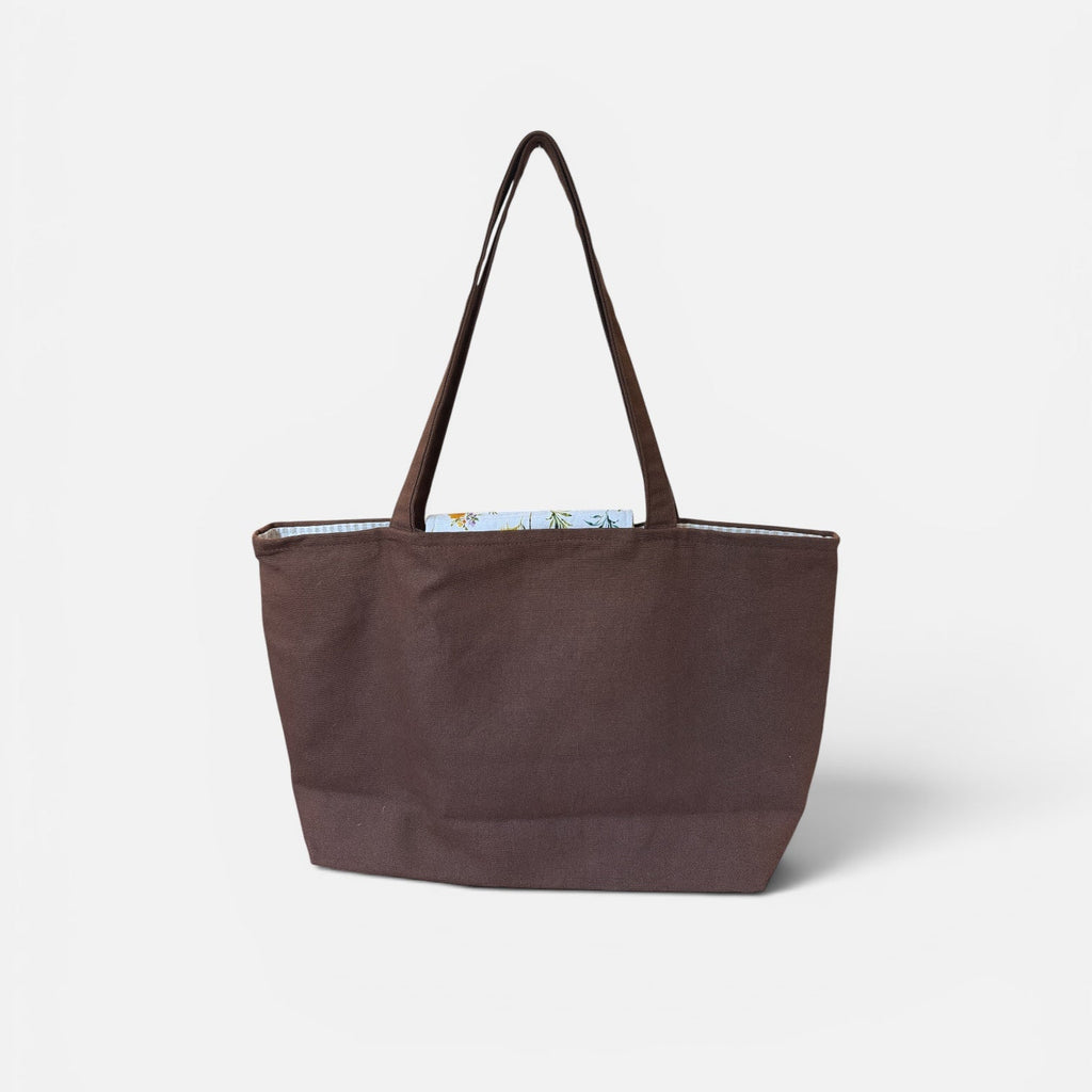 A dark brown canvas tote bag with matching shoulder straps, shown against a plain light gray background.