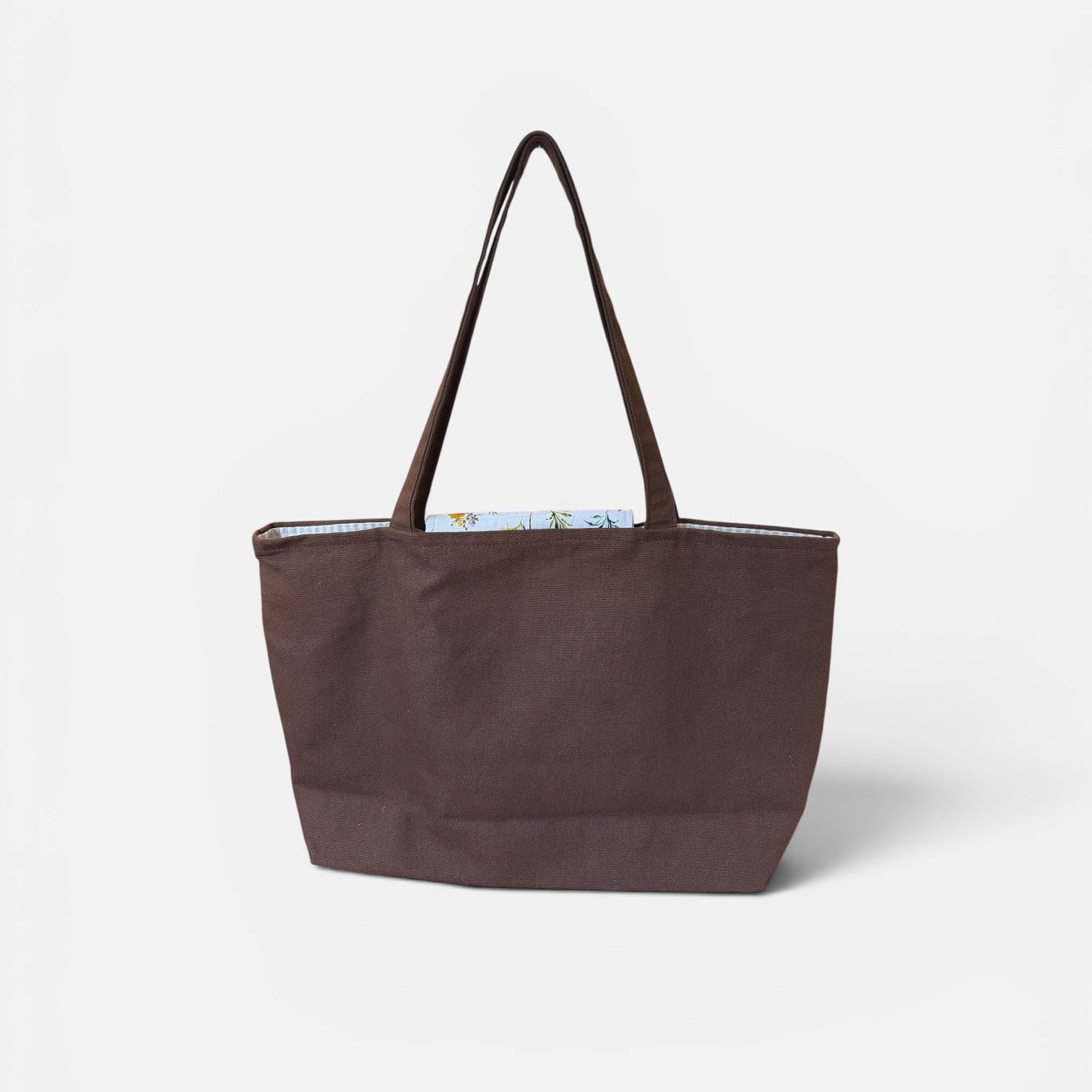 A dark brown canvas tote bag with matching shoulder straps, shown against a plain light gray background.