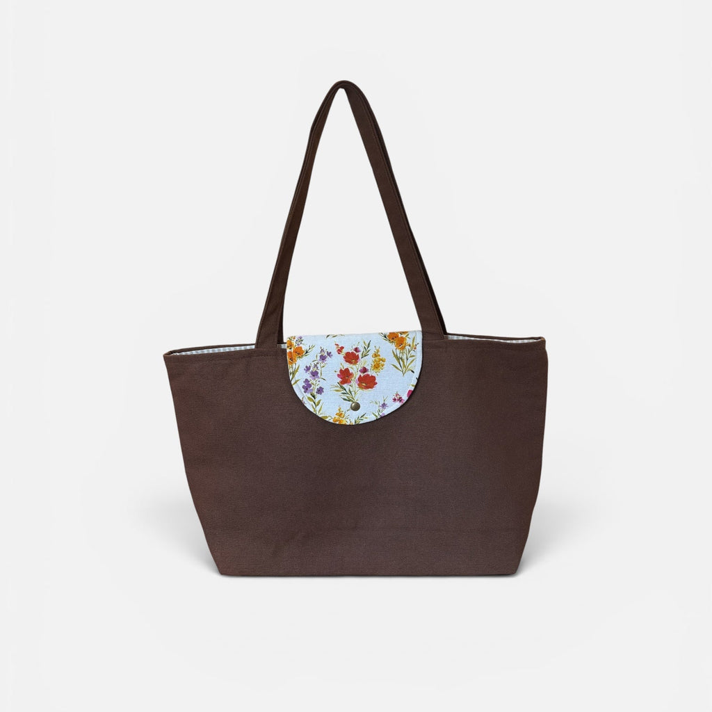 A dark brown tote bag with a floral-patterned semi-circular flap detail on the front and matching brown shoulder straps, shown against a plain light gray background.