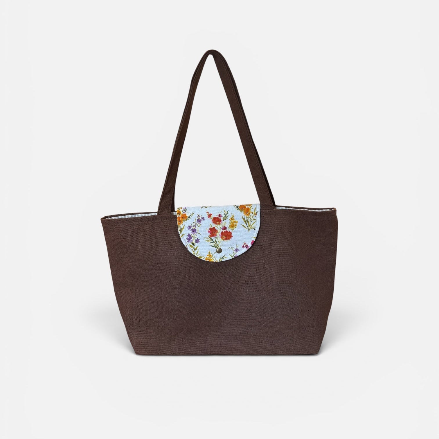 A dark brown tote bag with a floral-patterned semi-circular flap detail on the front and matching brown shoulder straps, shown against a plain light gray background.