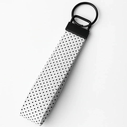 White polka dot fabric wristlet keychain with black hardware on a plain background