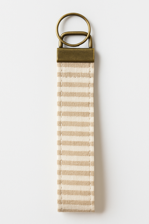 Neutral striped canvas wristlet keychain with brass hardware on white background