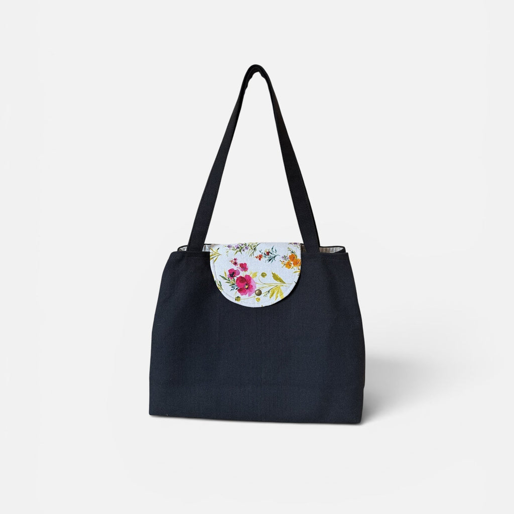 A black canvas tote bag with a floral-patterned circular flap detail on the front and black shoulder straps