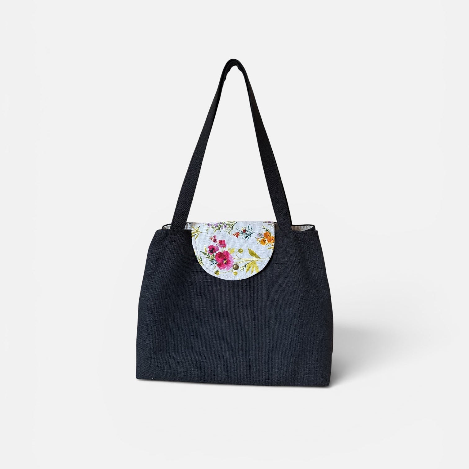 A black canvas tote bag with a floral-patterned circular flap detail on the front and black shoulder straps