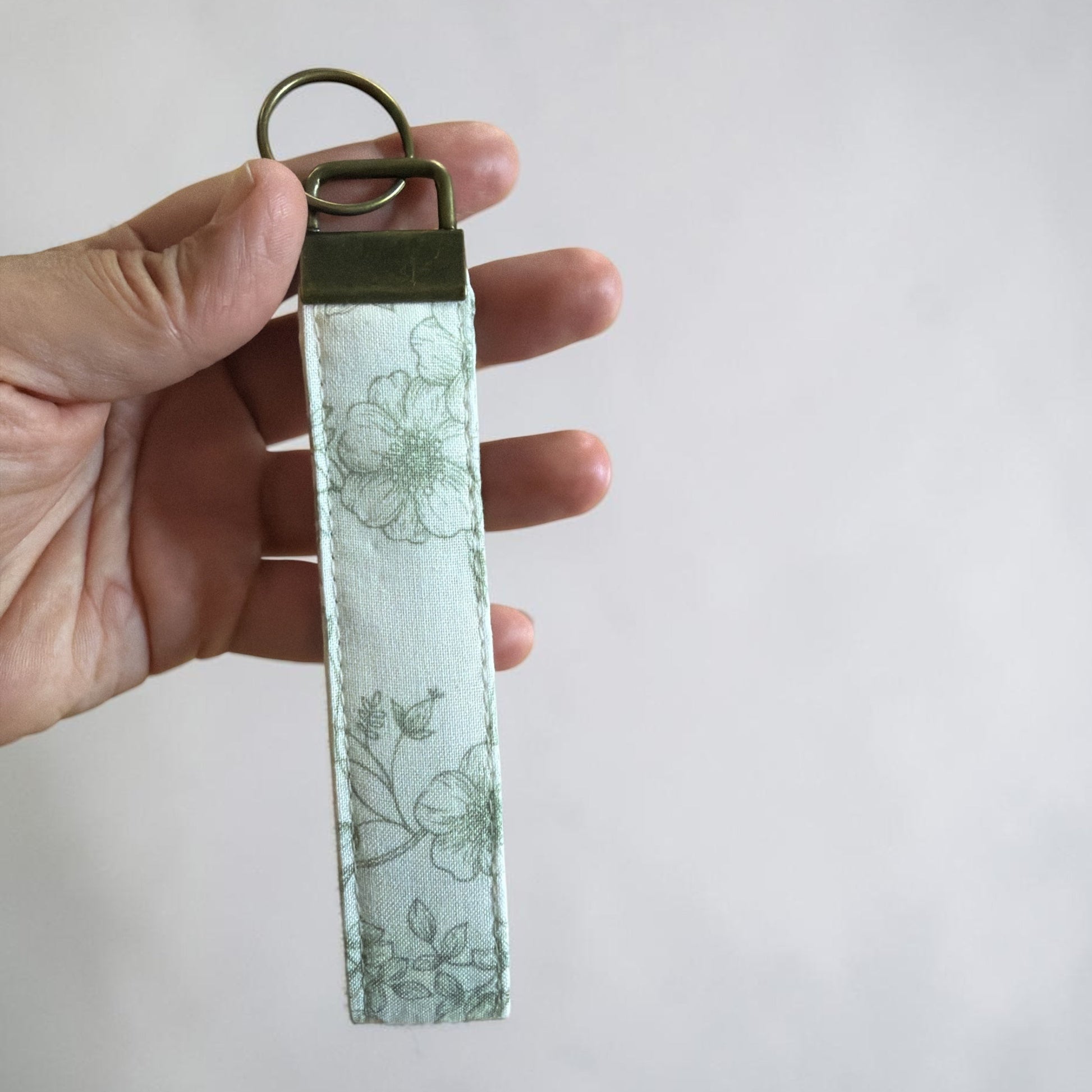 Hand holding a floral-patterned keychain against a plain background