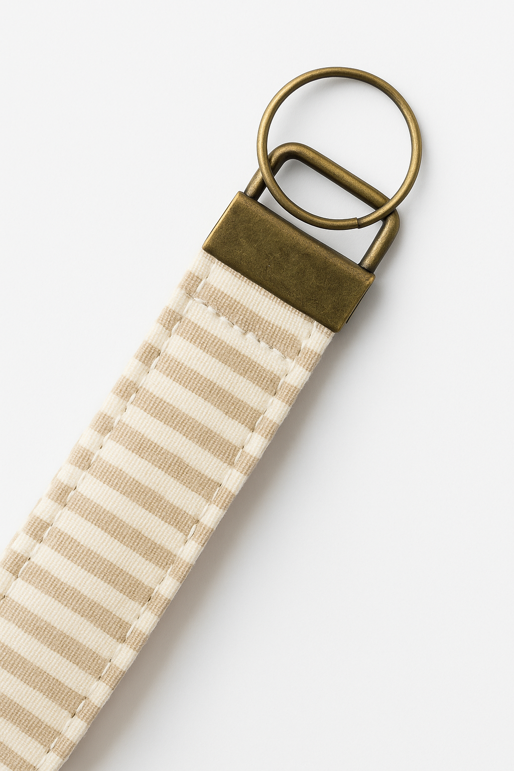 Beige and white striped canvas wristlet keychain with antique brass hardware on white background